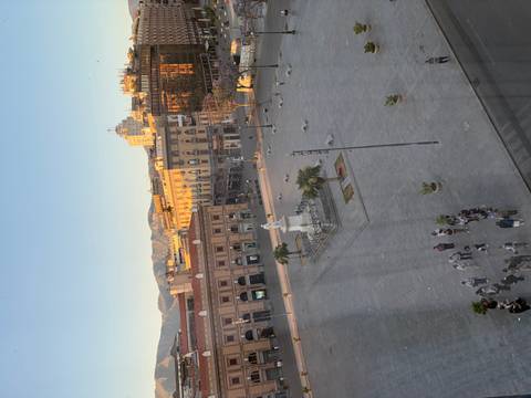 Elevated view of a grand city square with central statue and distant mountains in soft evening light