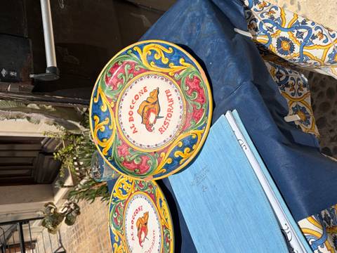 Decorative hand-painted ceramic plate reading 'Al Boccone Ristorante' displayed outside an eatery