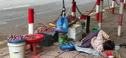 Street vendor rests beside baskets filled with purple passion fruits along a sidewalk market