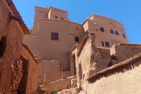 Upward perspective of mud-brick kasbah walls and decorative windows under a vivid blue sky.