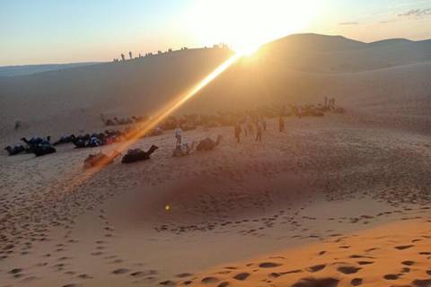 Visitors lie on sand dunes watching sunrise over the Sahara with sun rays streaking the lens.