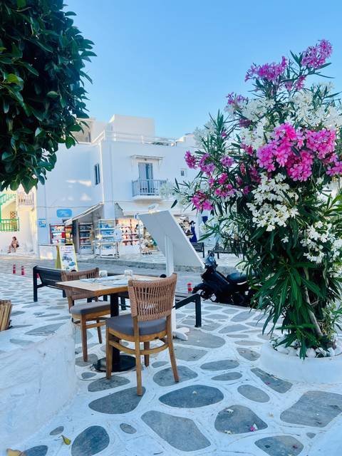 Charming outdoor restaurant table shaded by vibrant pink and white bougainvillea in a whitewashed Mykonos lane.