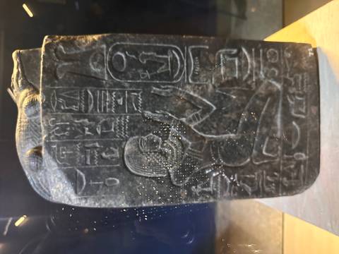 Ancient carved stela with hieroglyphs behind museum glass under soft lighting