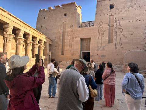 Guide explaining temple courtyard with tall relief-carved walls to a listening tour group