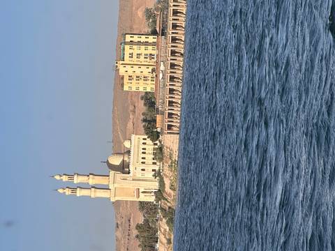 Elegant mosque with twin minarets overlooking blue waters and desert hills in background
