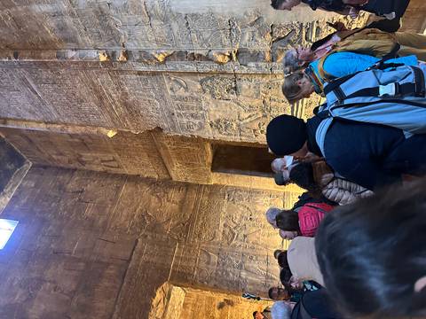 Crowd inside towering temple hall richly carved with hieroglyphs and lit from above
