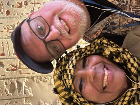 Close selfie of two happy travellers against a wall covered in ancient carvings