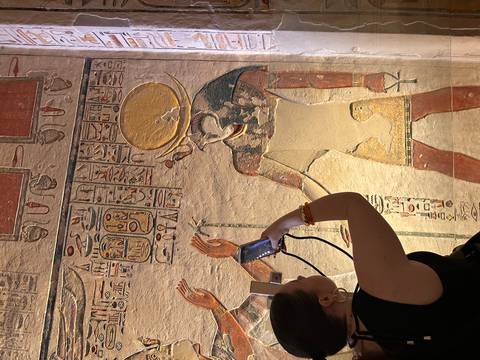Visitor photographing colorful wall painting of an Egyptian deity inside a tomb
