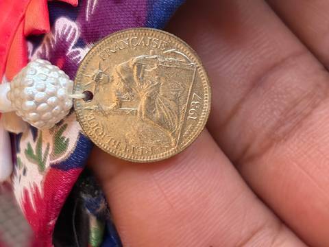 Macro shot of a 1937 French coin tied to colourful fabric on a hand.