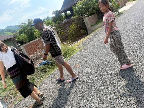 Candid street shot of three people walking on gravel lane beside village houses.