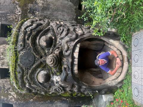 Tourist lying inside giant open-mouthed demon sculpture at Buddha Park surrounded by greenery.