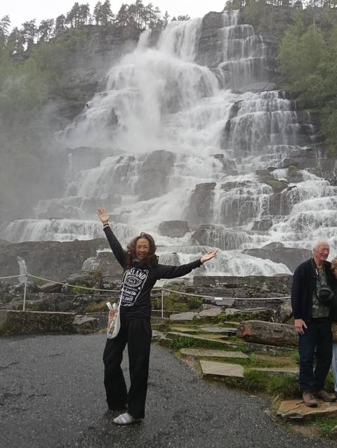 Tourist poses joyfully in front of roaring tiered waterfall with mist spraying everywhere.