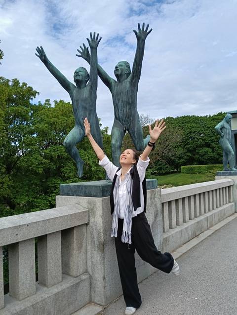 Smiling traveller lifts arms beside bronze statues in Oslo's Vigeland Sculpture Park.