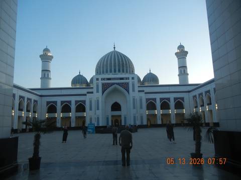 Spacious courtyard of grand white mosque with blue domes and tall minarets at dusk.
