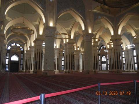 Lavish interior of grand mosque with tall columns, chandeliers and patterned carpet.