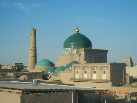 Skyline of Khiva with green-tiled domes and slender minaret glowing in morning light.