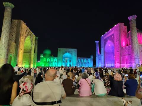 Nighttime light show bathes Samarkand's Registan in vibrant colours as crowd watches.