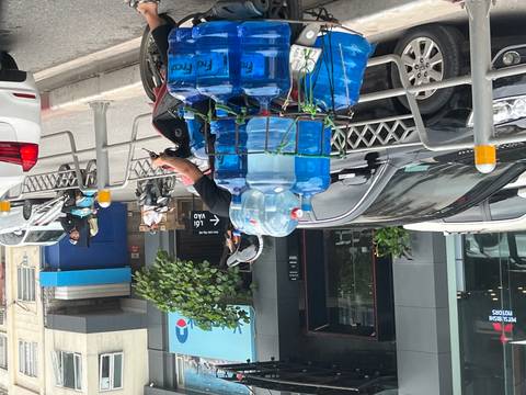 Motorcyclist transporting stacks of large blue water bottles along a busy city street.