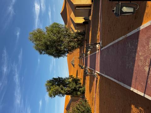Straight walkway leading to desert glamping tents amid orange dunes under blue sky.