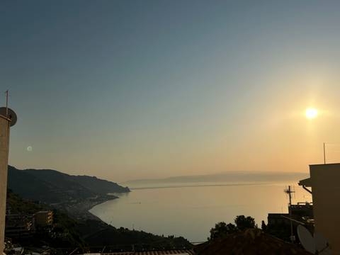 Hazy golden sunset over a calm sea and distant coastline viewed from a hilltop Sicilian town.