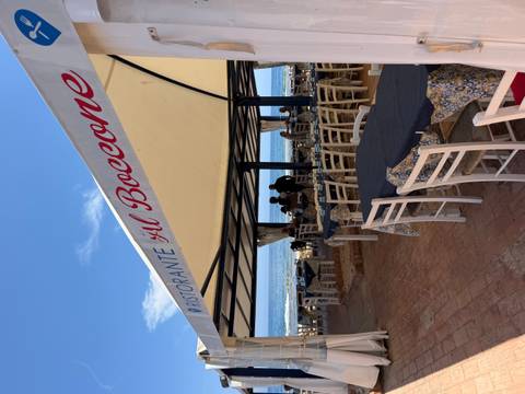 Open-air seaside restaurant with white chairs and a canvas roof overlooks gentle Mediterranean waves.
