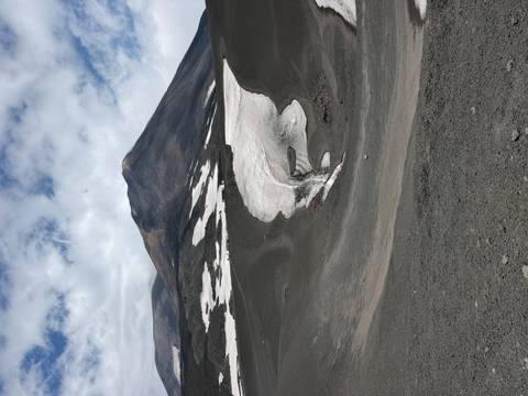 Volcanic slopes of Mount Etna with dark ash fields and lingering snow patches beneath dramatic clouds.
