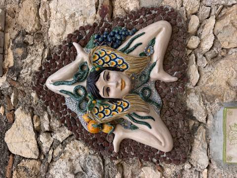 Close-up ceramic relief of the Sicilian Trinacria symbol embedded in a rustic stone wall.
