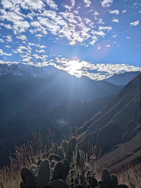 Bright sun breaks over Andean ridges casting lens flares and illuminating the rugged landscape.