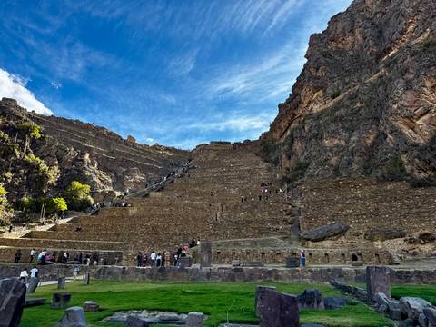Steep stone terraces of ancient Incan citadel rising against dramatic blue sky with scattered visitors