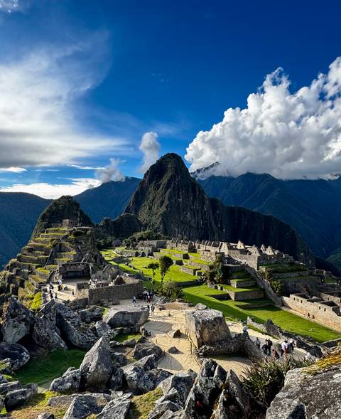 Iconic view of Machu Picchu ruins perched on ridge with Huayna Picchu peak and cloud-topped Andes behind