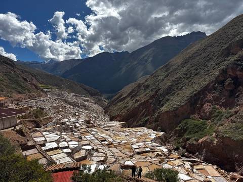 Expansive view of stepped salt evaporation ponds sprawling along a mountain valley under dramatic clouds