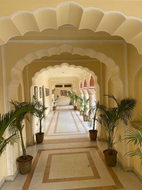 A long corridor with yellow scalloped arches, framed photos, and potted palms in a heritage building.