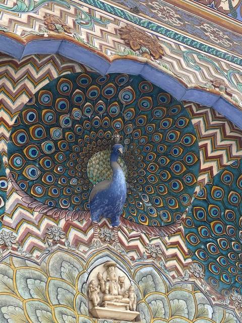 A vibrant Peacock Gate with intricate feather patterns and a sculpted peacock at Jaipur’s City Palace.