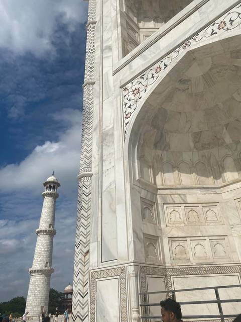 Detail of the white marble Taj Mahal archway with an elegant minaret set against a deep blue sky.
