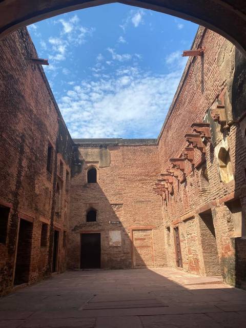Sunlit brick ruins with tall walls surrounding an open courtyard and a patch of blue sky above.