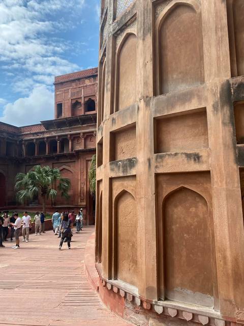Visitors explore a red-sandstone courtyard with tropical palms and high fortress walls.