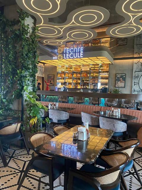 A stylish modern bar with a back-lit spirits display, lush greenery, and diners seated at tables.