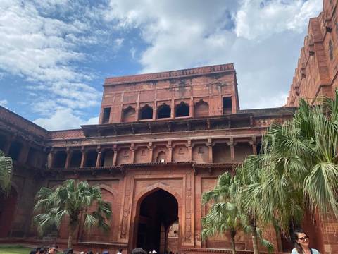 An inner courtyard façade of red-sandstone arches and balconies set against a cloudy sky.