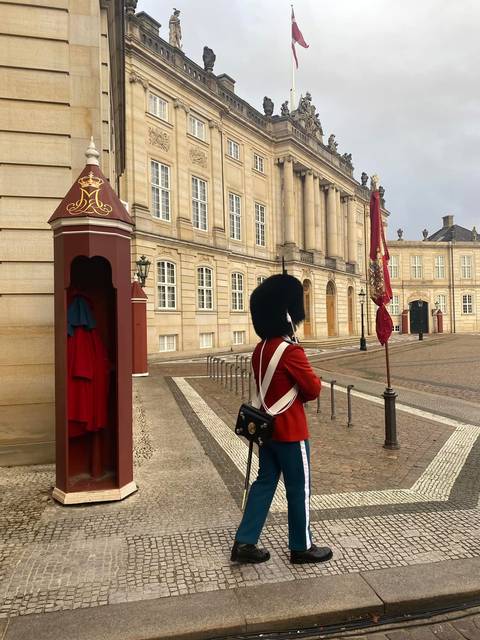 A royal guard in red uniform and bearskin hat stands watch at the cream-stone Amalienborg Palace.