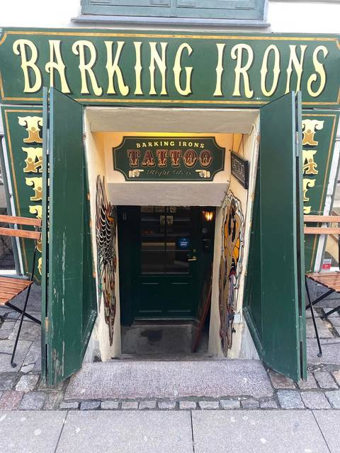 A narrow stairwell descends to a vintage-styled tattoo parlor with ornate painted signage.