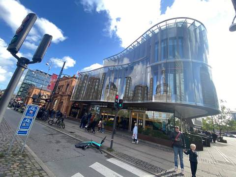 A curved glass building reflects city life on a bustling Copenhagen street with cyclists and pedestrians.