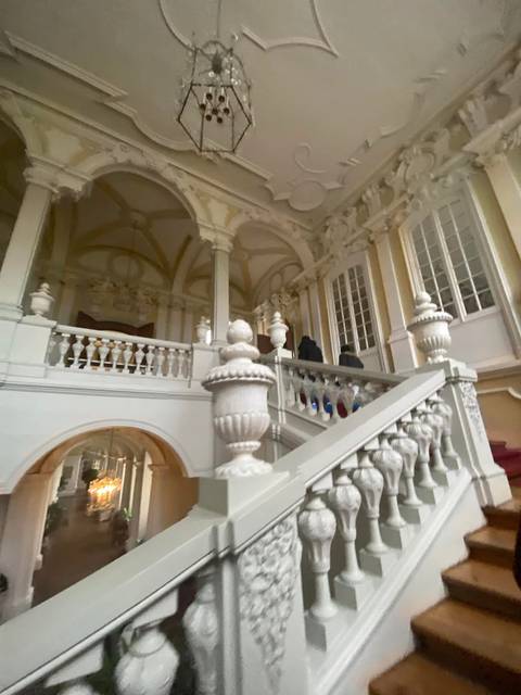 A motion-blurred grand staircase with ornate balustrades inside a baroque palace.