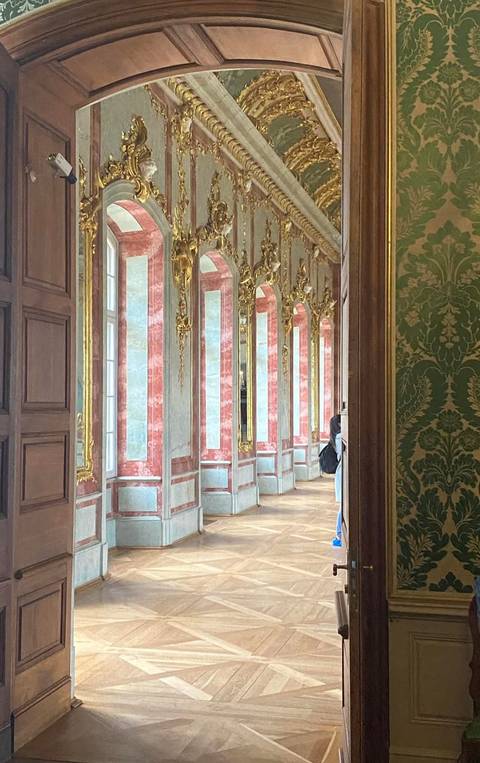 A long gilded corridor with red and white marble walls, tall mirrors, and baroque details.
