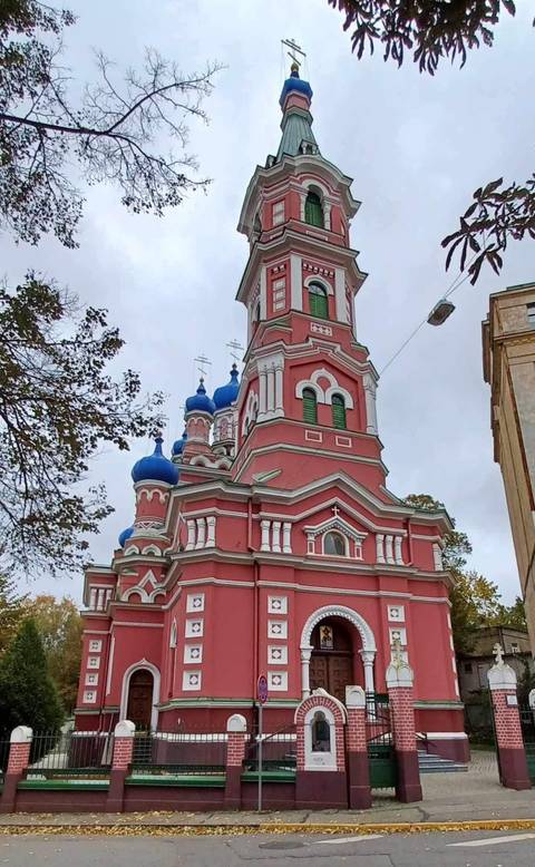 A striking pink orthodox church with blue onion domes and white trim set against a gray sky.