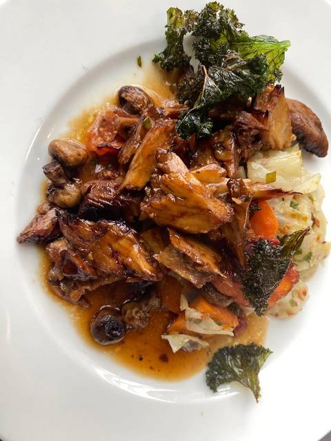 Close-up of a hearty roasted meat dish with vegetables on a white plate.