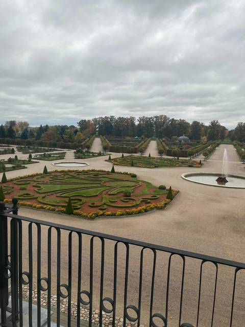 Formal baroque gardens with symmetrical hedges, fountains, and tree-lined alleys viewed from a terrace.