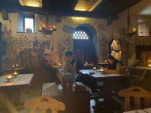 Dimly lit medieval-style tavern interior with candles and patrons reading menus.