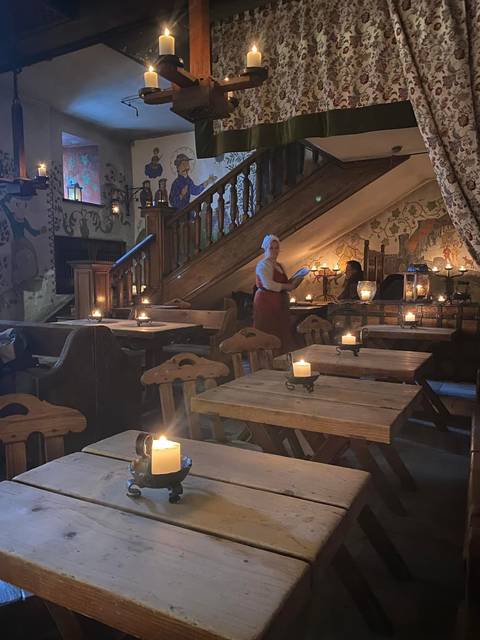Waitress in period costume carries candles inside a rustic medieval tavern.