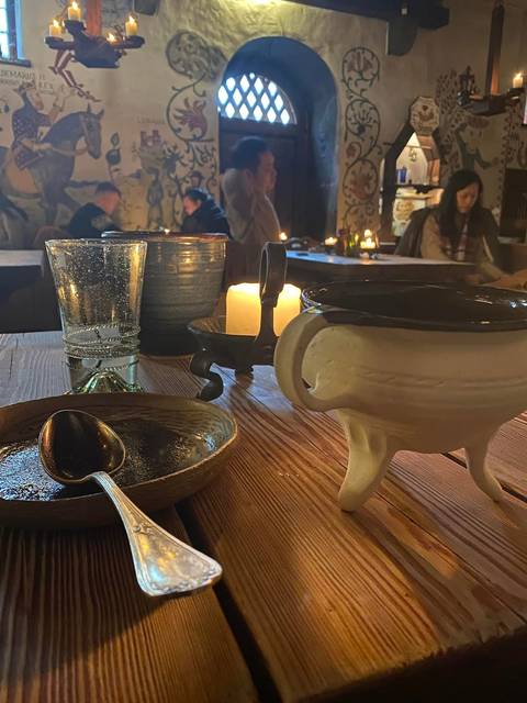 Rustic wooden table with candlelight, ceramic bowl, glass and spoon in a medieval eatery.