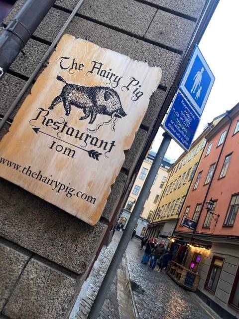 Wooden restaurant sign featuring a wild boar and narrow Stockholm street in the background.